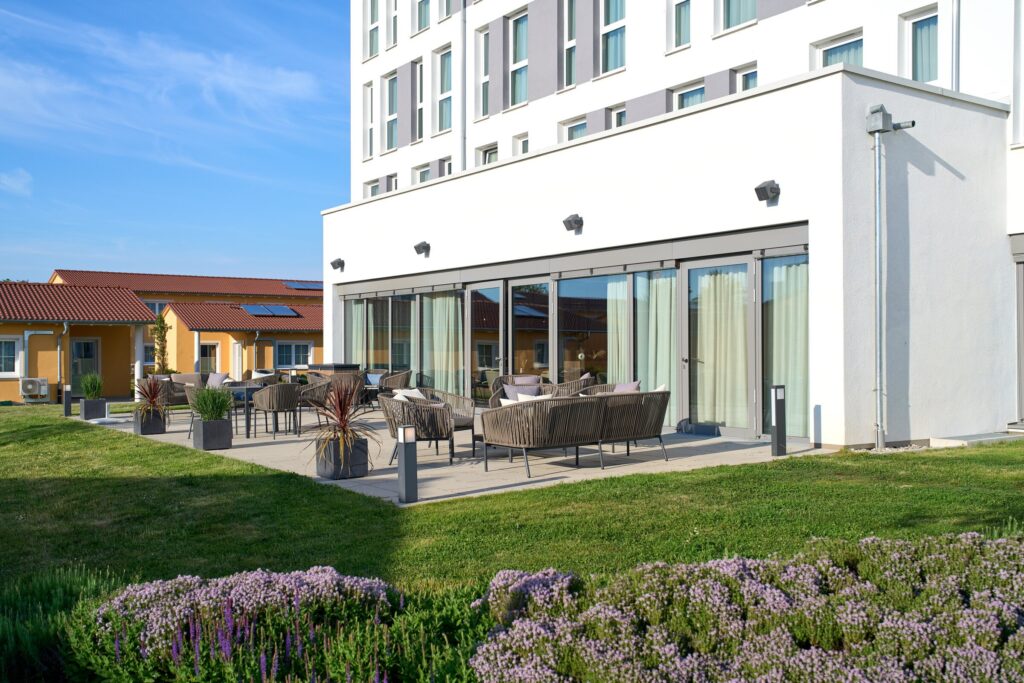Terrasse eines Hotels mit mehreren Sitzgelegenheiten und Pflanzen in Töpfen.