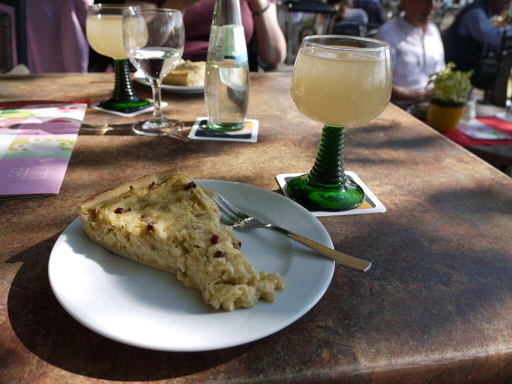 Ein Glas Federweißer und ein Stück Zwiebelkuchen auf einem Holztisch