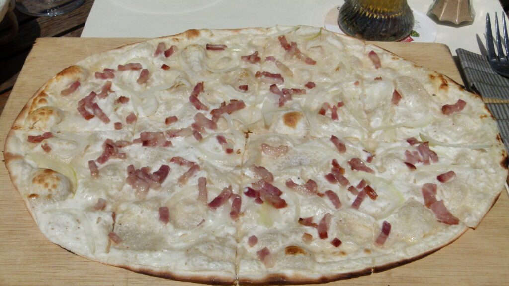 Elsässer Flammkuchen mit Crème fraîche, Zwiebeln und Speck auf einem Holzbrett
